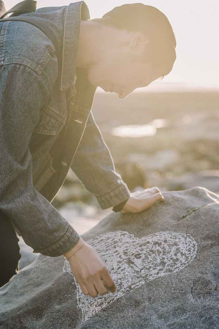 man sketching heart on a gray rock